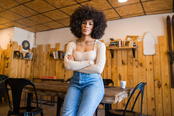 Confident young woman with afro hair leaning on table