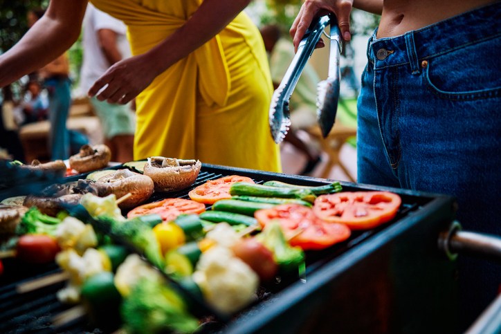 Two women preparing and grilling vegetables at an outdoor barbecue party. Social gathering with food. Summer cooking and celebration concept. Meat free shot.