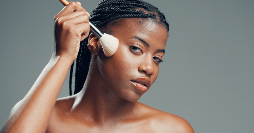 Makeup, aesthetic and portrait of black woman with brush in studio for beauty, foundation or glow. Face, apply cosmetics or model with product for makeover, change and powder on gray background space