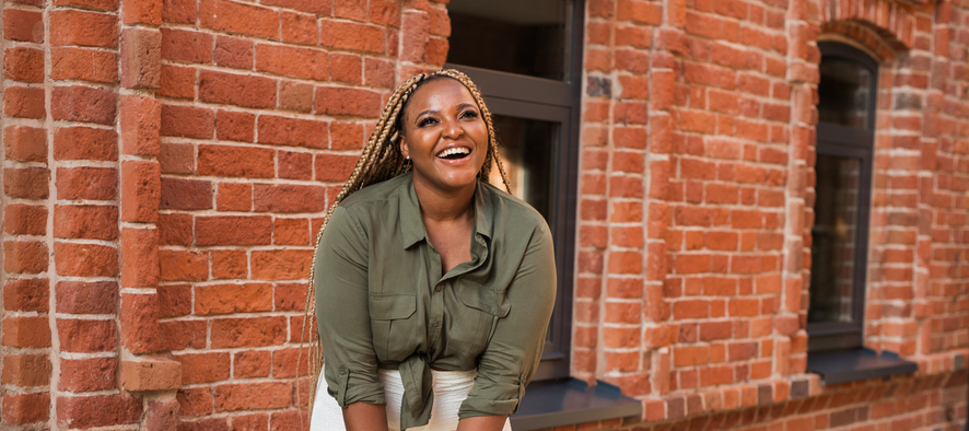 African american woman laughing joyfully while standing on a city street on a sunny day. Freedom, positivity, and happiness in an urban environment. Banner with copy space