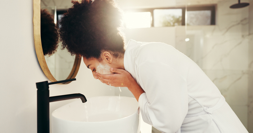 Woman, water and wash face for skincare in bathroom, acne control and cleansing routine at mirror. African person, dermatology and soap in home for facial treatment, skin hydration and exfoliation