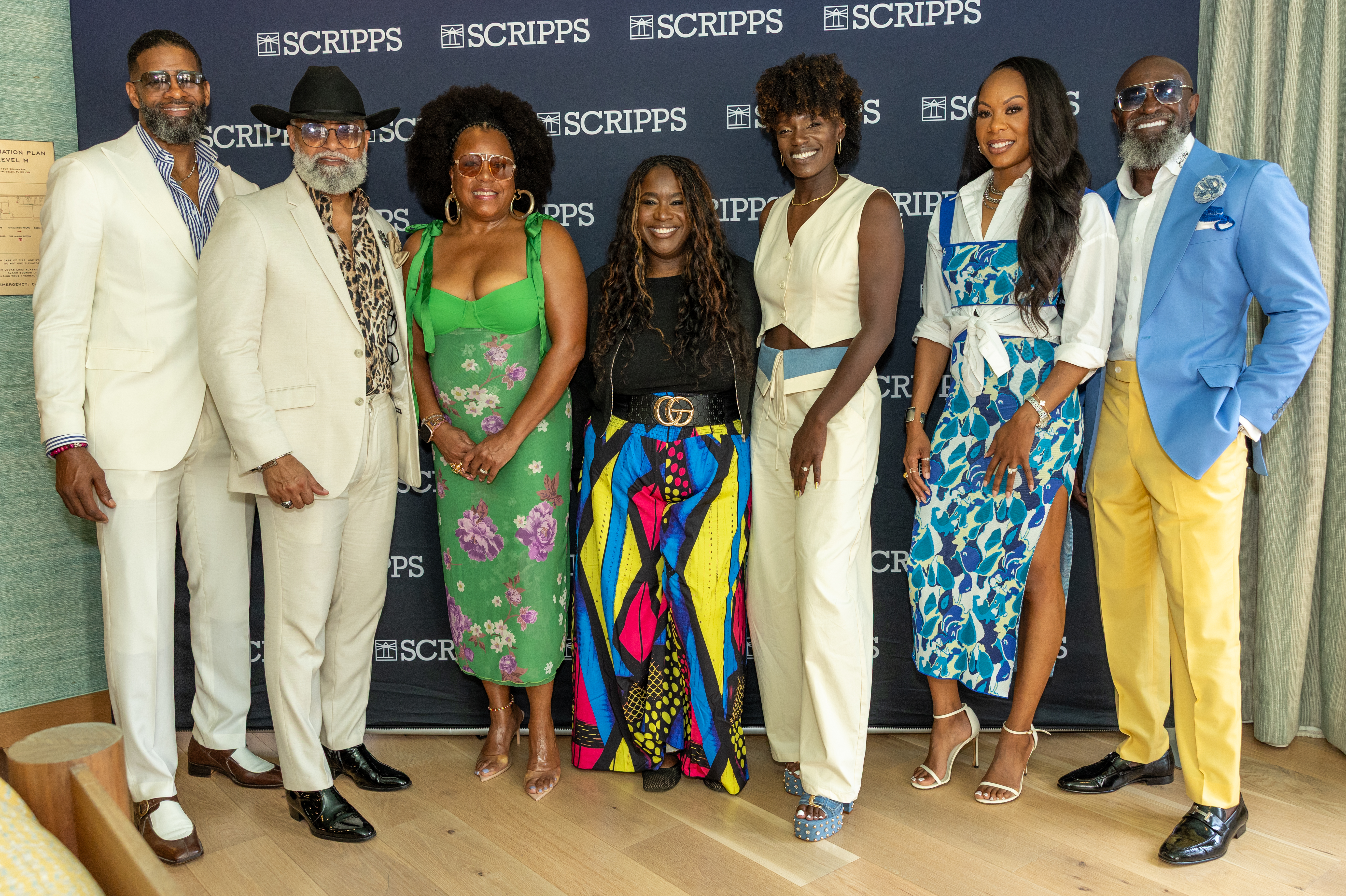 A group of six people posing in front of a Scripps backdrop, dressed in colorful, stylish outfits.