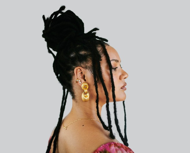 Serene African American Woman With Dreadlocks in Profile Wearing Gold Earrings and Pink Top