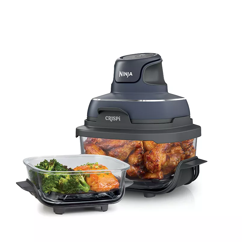 A black Ninja Crispi food processor with a glass bowl containing cooked food and a separate container with greens.