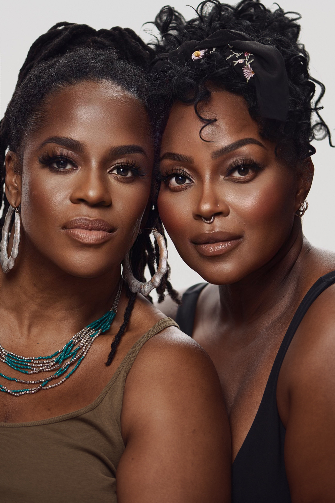 Two women with intricate hairstyles and makeup, wearing jewelry and looking directly at the camera.