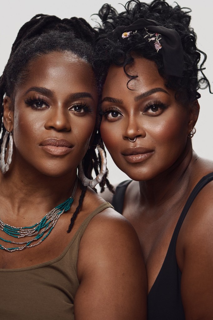 Two women with intricate hairstyles and makeup, wearing jewelry and looking directly at the camera.