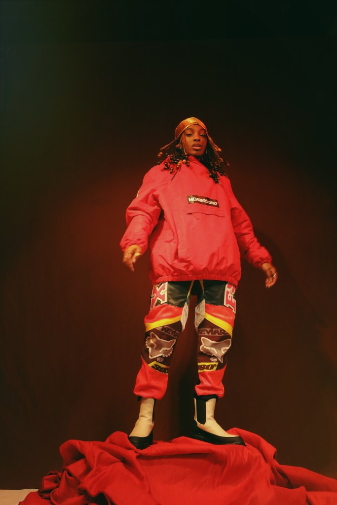 A person wearing a bright red hooded jacket with "MEMBERS ONLY" printed on it, standing in a dark, dramatic setting.