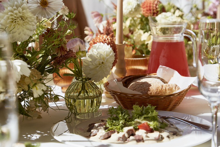 Restaurant summer aesthetics table setting, flowers arrangement under sunlight shadows. Cozy setup with flowers and candles