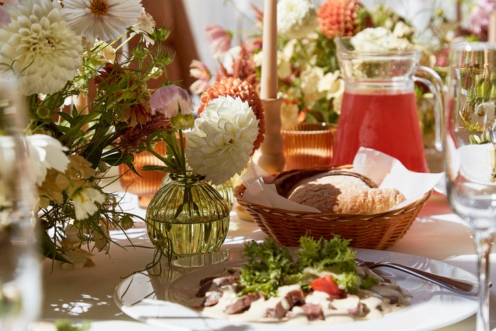 Restaurant summer aesthetics table setting, flowers arrangement under sunlight shadows. Cozy setup with flowers and candles