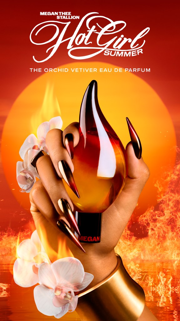 A close-up of a hand holding a glass bottle with an orchid-themed fragrance label against a fiery orange background.