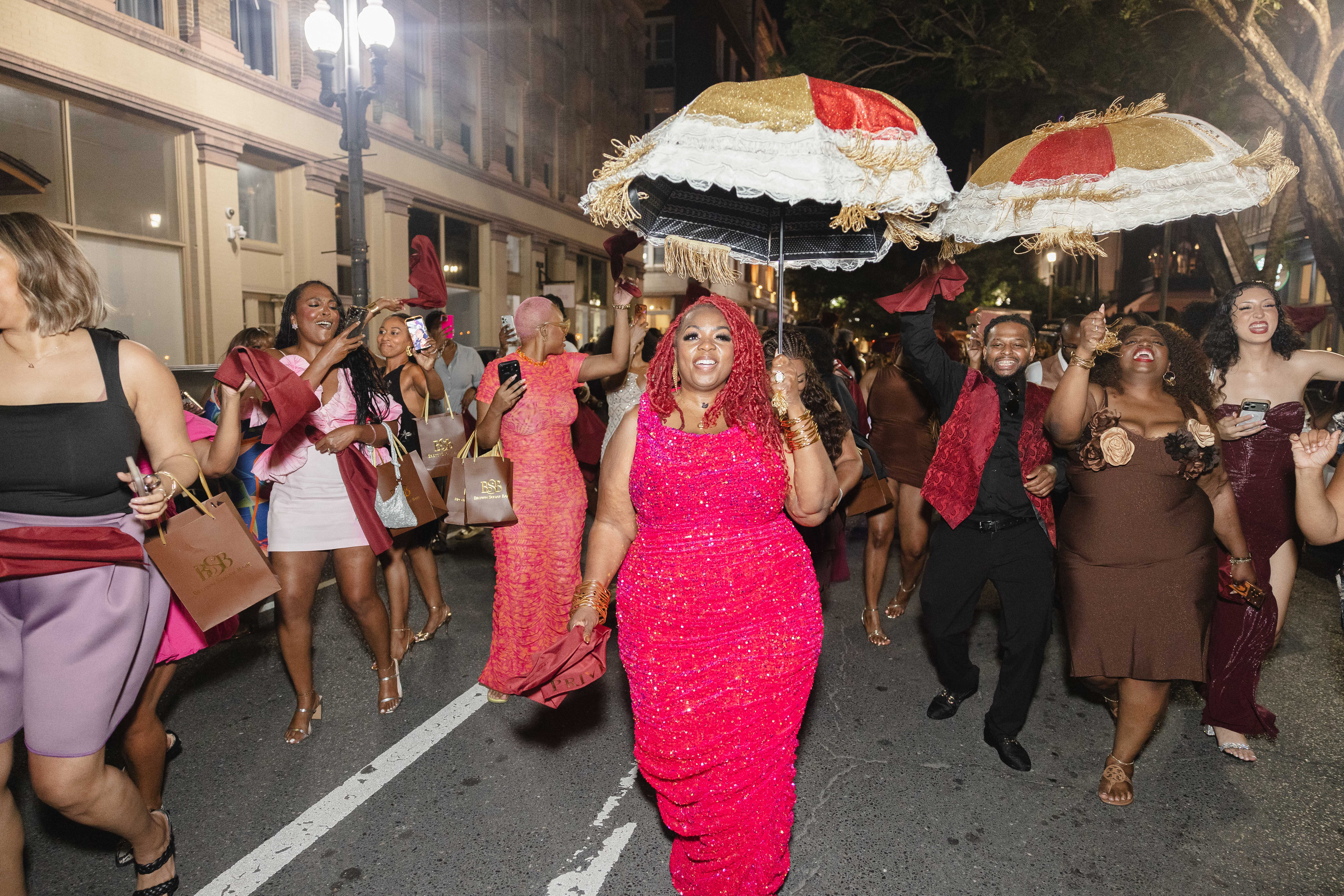 A group of people in colorful, festive attire celebrating at night on a city street, with large decorative umbrellas overhead.