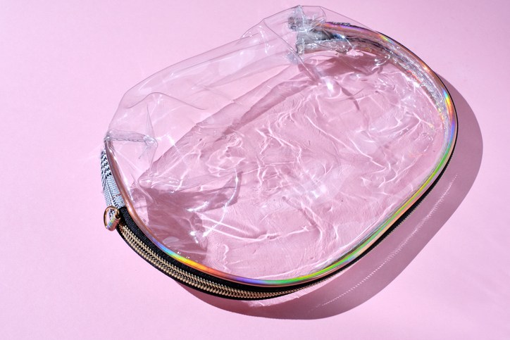 Empty plastic transparent bag for cosmetics on a trendy pink background with shadows and sunlight. Transparent makeup bag in flat style. Flat style
