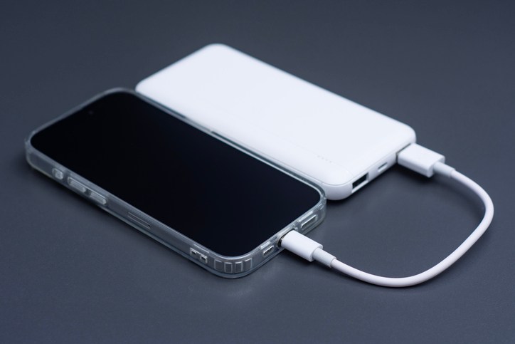 Mobile phone connected to white external power bank with usb cable on dark background. Portable backup battery charging smartphone screen mockup for travel, technology or emergency energy.