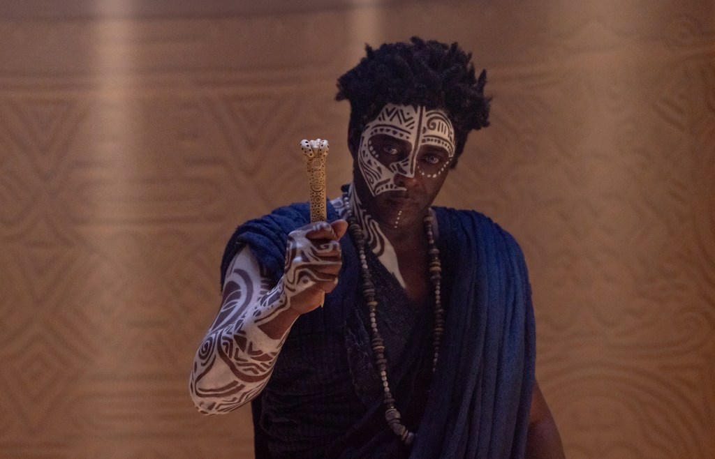 A person wearing face paint and holding a staff in a dimly lit setting.