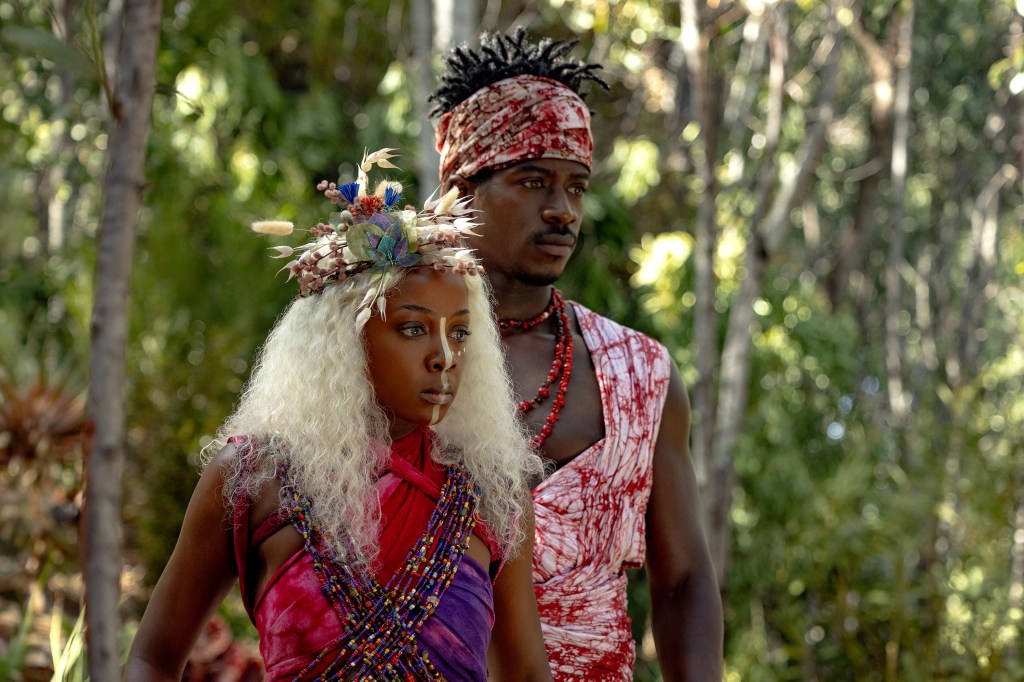 Two people in colorful traditional African attire standing in a lush forest setting.