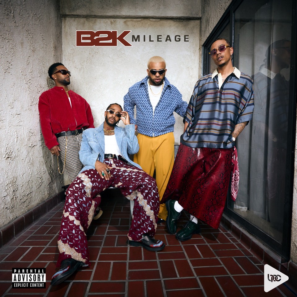 Four people wearing stylish outfits stand in front of a wall with the "B2K MILEAGE" logo.