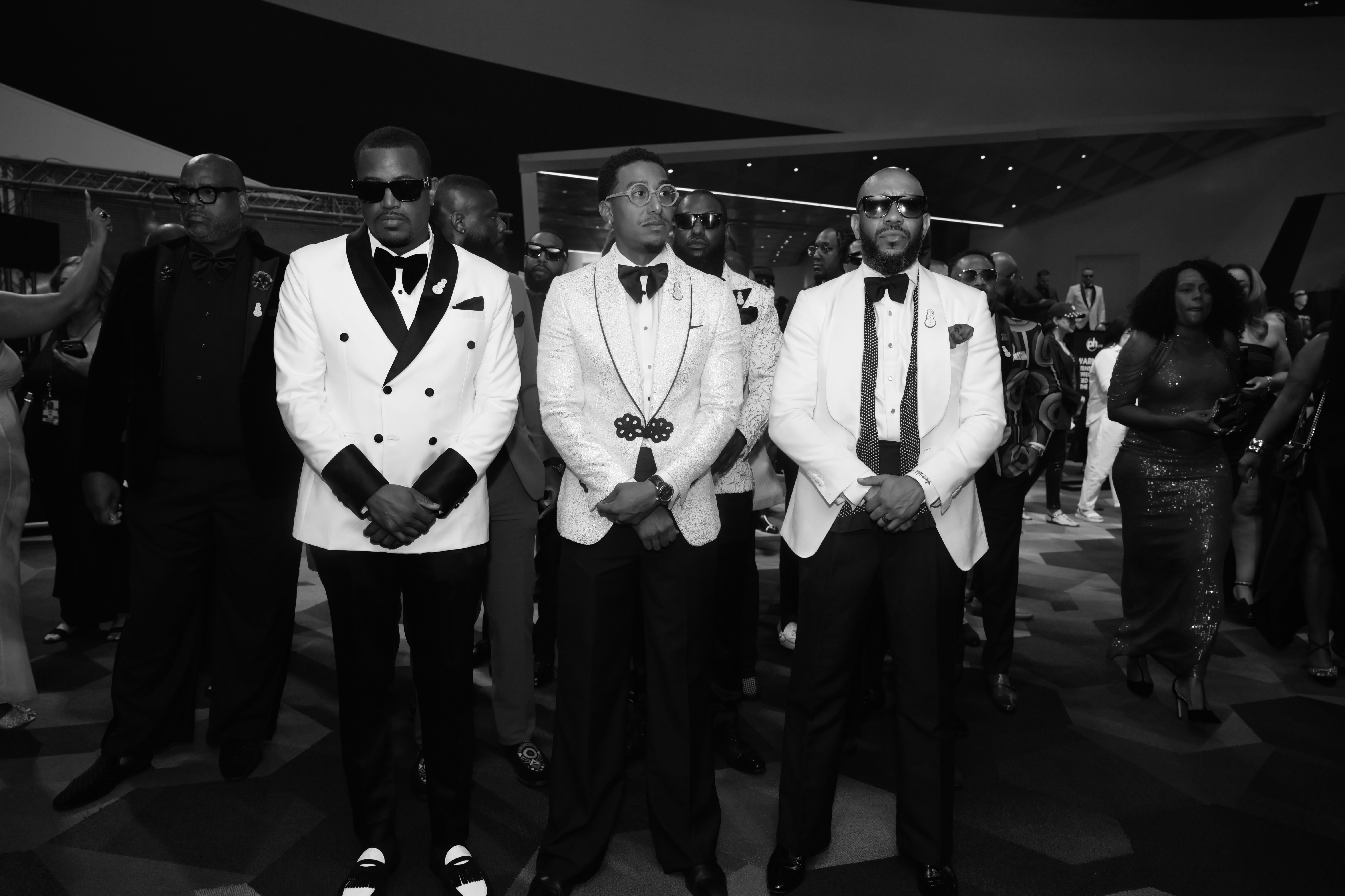 A group of well-dressed Black men in formal attire, including tuxedos and bow ties, posing together at a formal event.